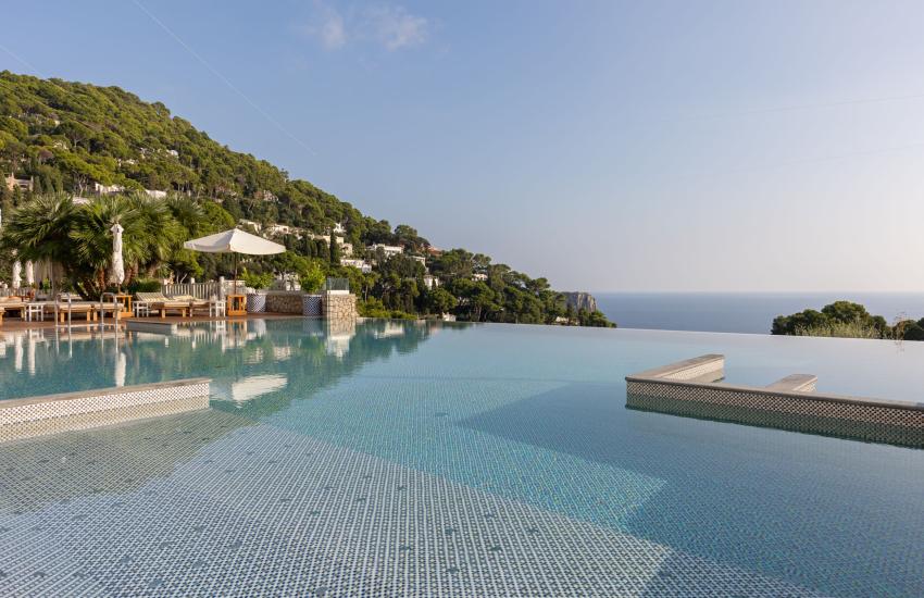 Piscina a sfioro con vista mare e colline verdi.