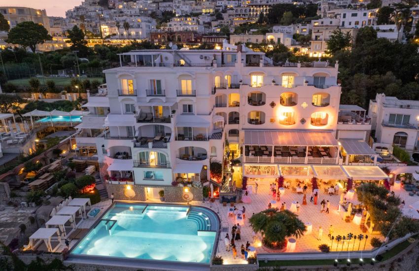 Vista notturna di un hotel con piscina e terrazza illuminata.